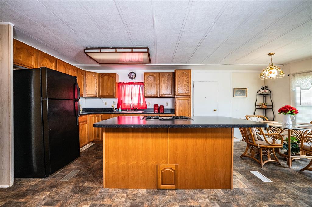 A kitchen features wood cabinets, a black refrigerator, a central island with a cooktop, and flooring — 3011 SUN WAY, LAKELAND, FL