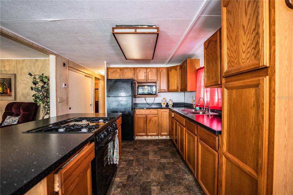 A kitchen with wood cabinets, black countertops, a gas cooktop, and a black refrigerator — 3011 SUN WAY, LAKELAND, FL