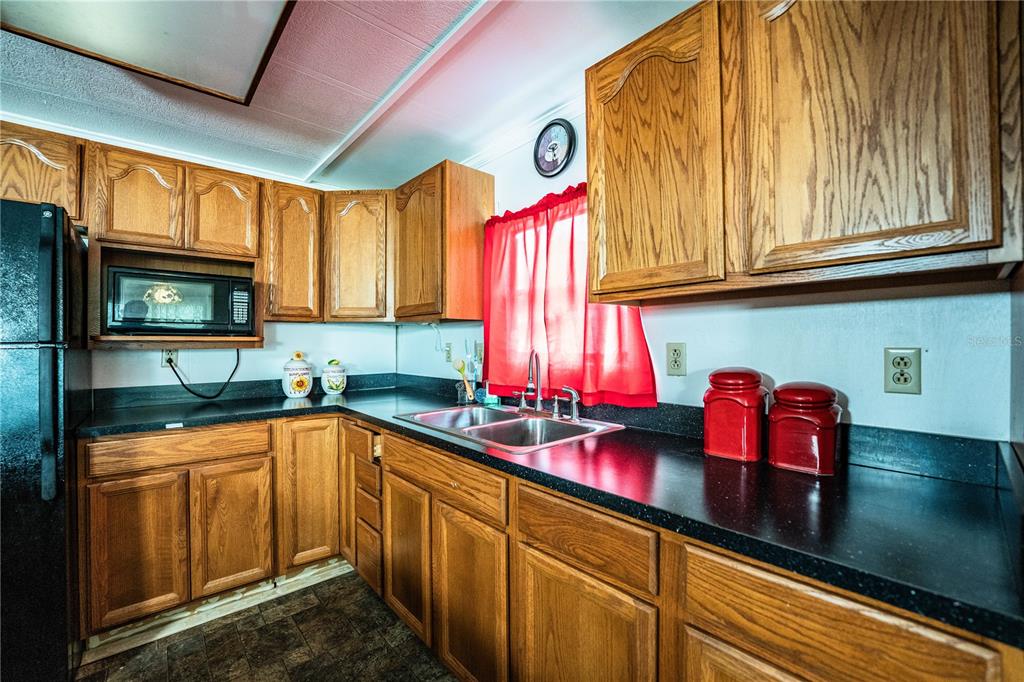 A kitchen with oak cabinets, black countertops, a double sink, and red window curtains — 3011 SUN WAY, LAKELAND, FL