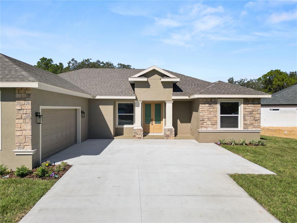 A single-story house with a tan stucco exterior, stone accents, and a concrete driveway — 4300 CREMONA DRIVE, SEBRING, FL