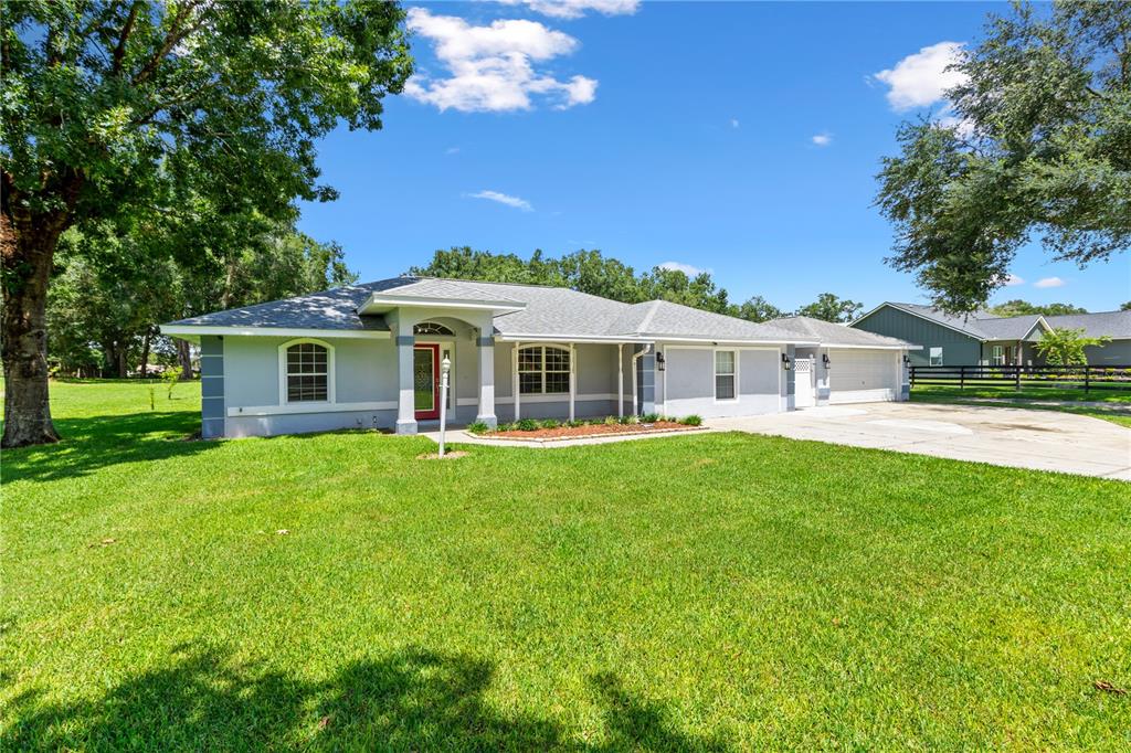 A single-story house with a gray exterior, red front door, and a large front lawn — 2607 SE 156TH PLACE ROAD, SUMMERFIELD, FL