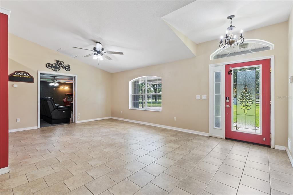 A spacious living room with beige tile floors, a ceiling fan, and a red front door — 2607 SE 156TH PLACE ROAD, SUMMERFIELD, FL