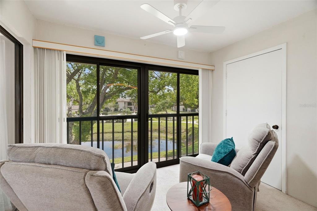 A sunroom with two armchairs, a ceiling fan, and sliding glass doors overlooking a pond — 2700 NEBRASKA AVENUE UNIT 2-203, PALM HARBOR, FL