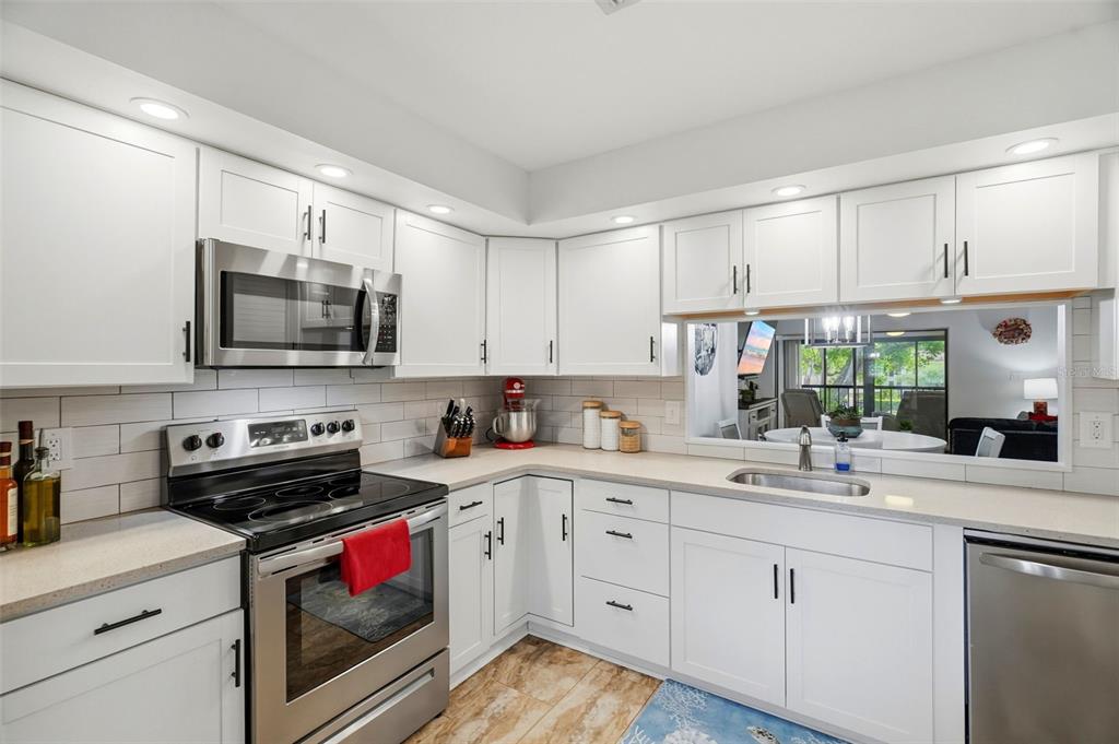 A kitchen with white cabinets, stainless steel appliances, light countertops, and a pass-through window — 2700 NEBRASKA AVENUE UNIT 2-203, PALM HARBOR, FL