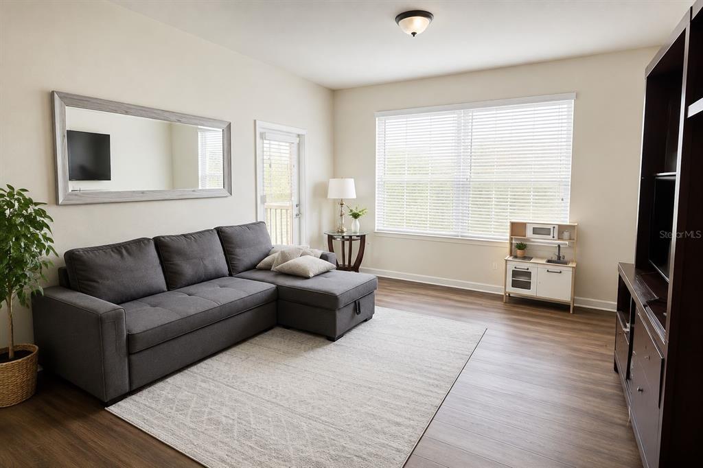 A living room features a gray sectional sofa, a large mirror, and wood-look flooring — 3338 ROBERT TRENT JONES DRIVE UNIT 410, ORLANDO, FL