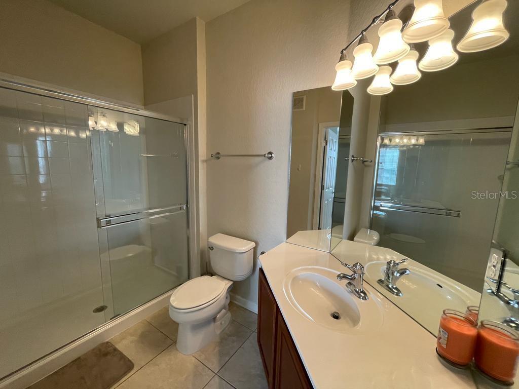 A bathroom features a glass-enclosed shower, a white toilet, and a vanity with a mirror — 3338 ROBERT TRENT JONES DRIVE UNIT 410, ORLANDO, FL