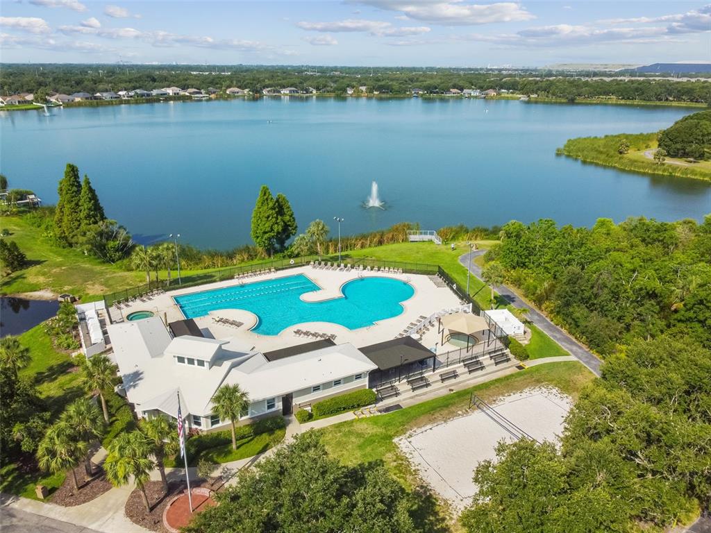 An aerial view shows a community swimming pool, clubhouse, and sand court beside a lake — 6637 THACKSTON DRIVE, RIVERVIEW, FL