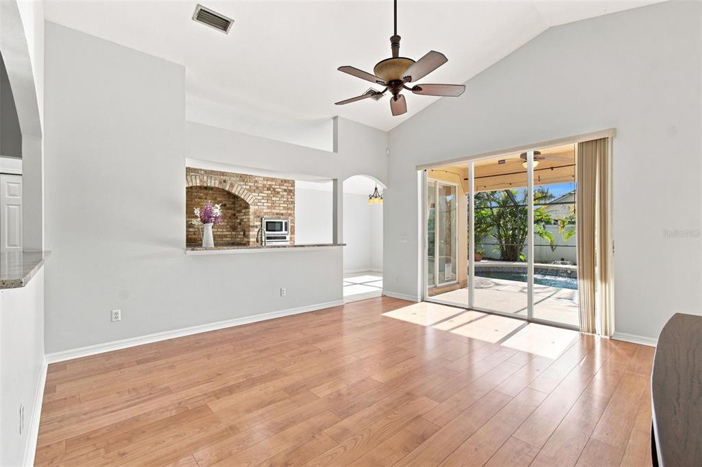 A living room with wood-look flooring, a brick-accented kitchen pass-through, and sliding glass doors — 6637 THACKSTON DRIVE, RIVERVIEW, FL