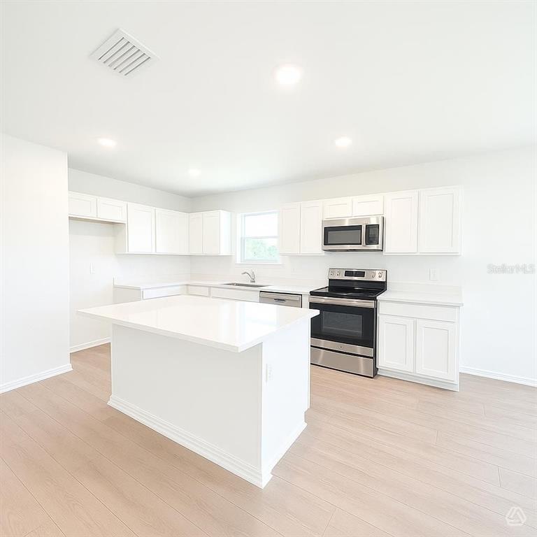 A modern kitchen features white cabinets, a central island, and stainless steel appliances — 12922 RED DEER PLACE, PARRISH, FL