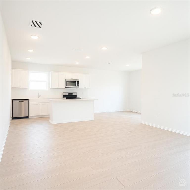 A modern kitchen with white cabinetry and light wood flooring opens into a living area — 12922 RED DEER PLACE, PARRISH, FL