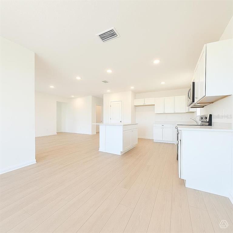 A bright, open-concept kitchen and living area features white cabinetry, an island, and light flooring — 12922 RED DEER PLACE, PARRISH, FL