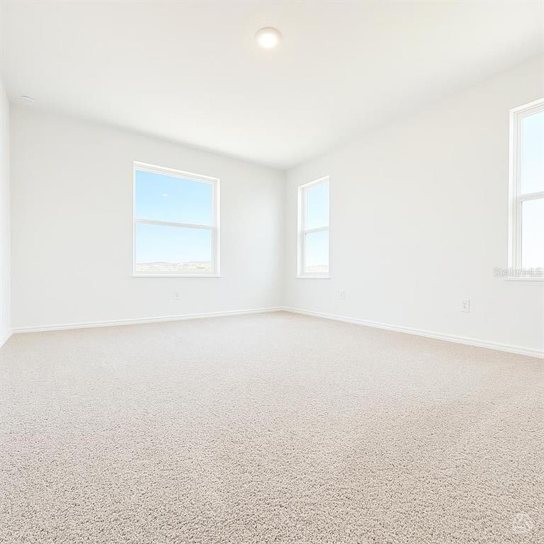 An empty room with white walls, beige carpet, and three windows — 12922 RED DEER PLACE, PARRISH, FL