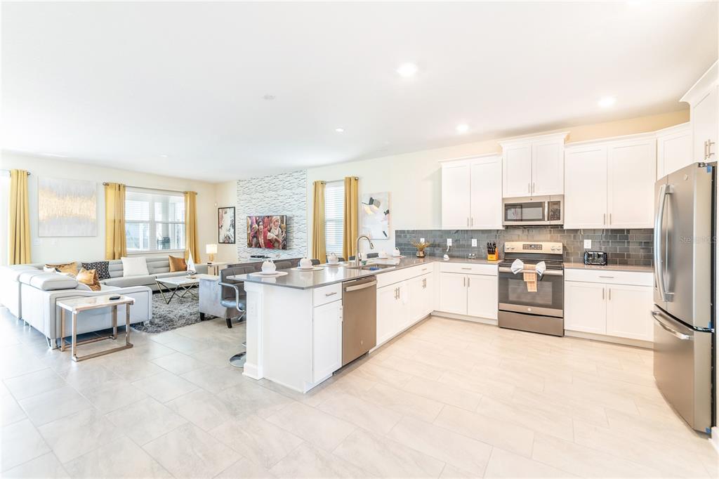 An open-concept kitchen and living area features white cabinetry, stainless steel appliances, and tile flooring — 8888 CABOT CLIFFS DRIVE, DAVENPORT, FL
