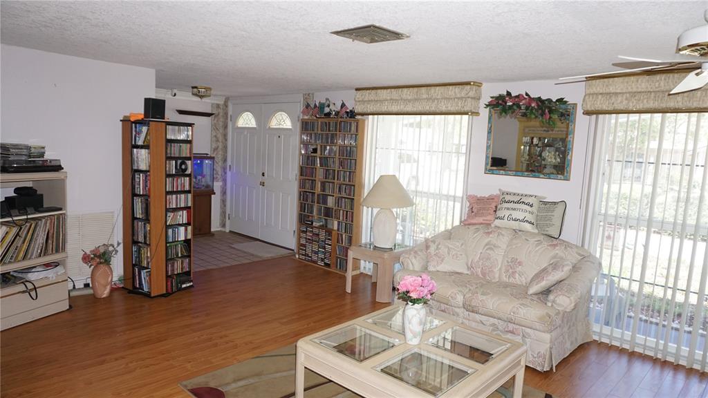 A living room features wood-look flooring, a floral sofa, a glass-top coffee table, and bookshelves — 12507 STONE HOUSE LOOP, HUDSON, FL