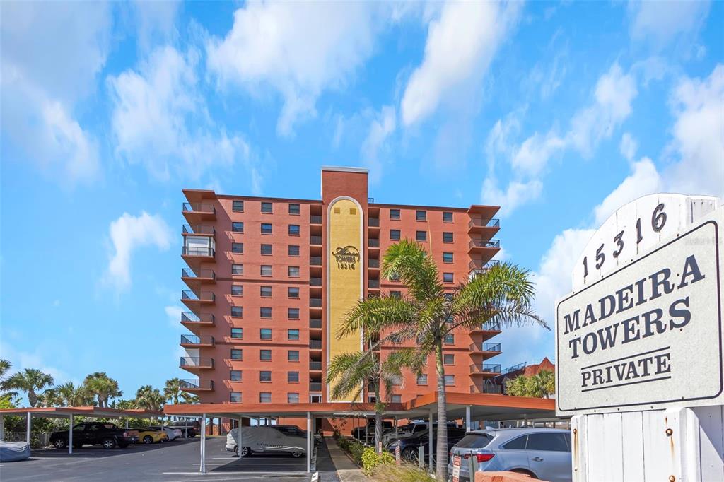 A multi-story brick apartment building stands behind a parking lot with a prominent sign — 15316 GULF BOULEVARD UNIT 604, MADEIRA BEACH, FL