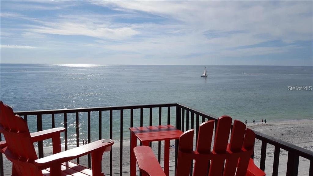 A balcony with red Adirondack chairs and a table overlooks the ocean and beach — 15316 GULF BOULEVARD UNIT 604, MADEIRA BEACH, FL