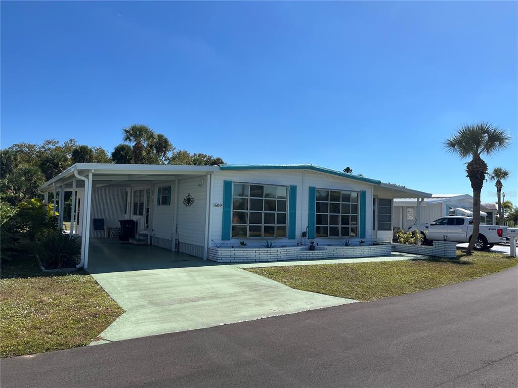 A white manufactured home features a carport, teal shutters, and a paved driveway — 609 CERVINA DRIVE, VENICE, FL