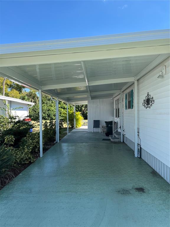A covered carport with a painted green concrete floor sits beside a white mobile home — 609 CERVINA DRIVE, VENICE, FL