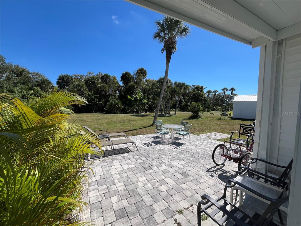 A paved patio features outdoor furniture and a tricycle overlooking a large, grassy backyard — 609 CERVINA DRIVE, VENICE, FL