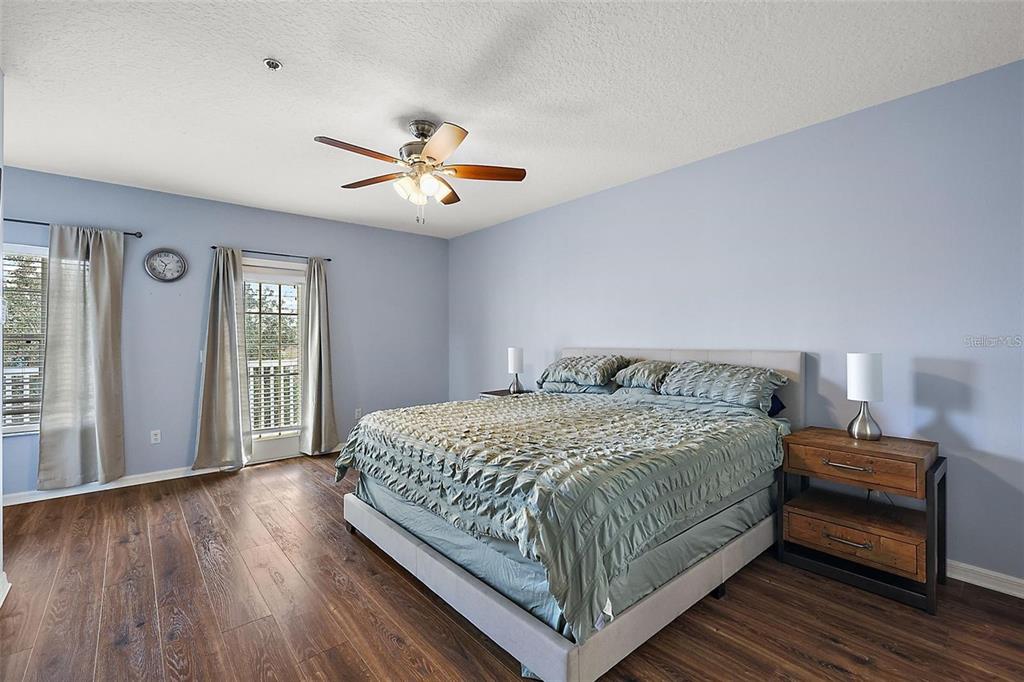 A bedroom features light blue walls, wood-look flooring, a ceiling fan, and a king-sized bed — 412 BLUE BAYOU LANE, WINTER SPRINGS, FL