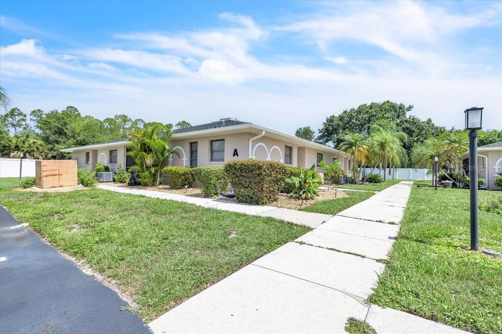 A single-story building with a beige exterior and a sidewalk leading to unit A — 24540 HARBORVIEW ROAD UNIT A3, PUNTA GORDA, FL