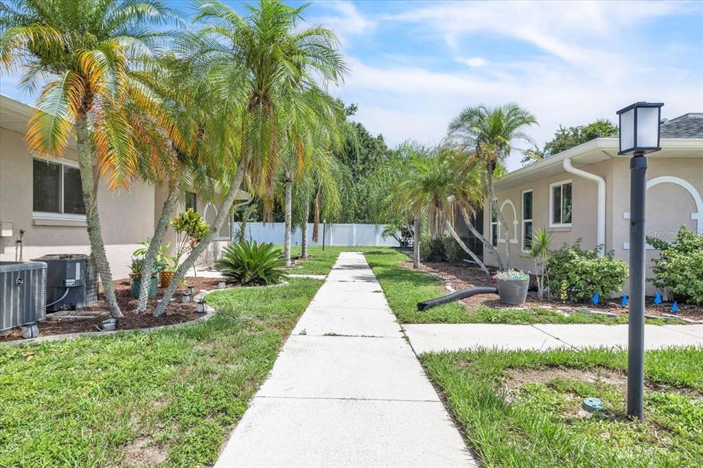 A concrete walkway leads between two residential buildings surrounded by palm trees and landscaping — 24540 HARBORVIEW ROAD UNIT A3, PUNTA GORDA, FL