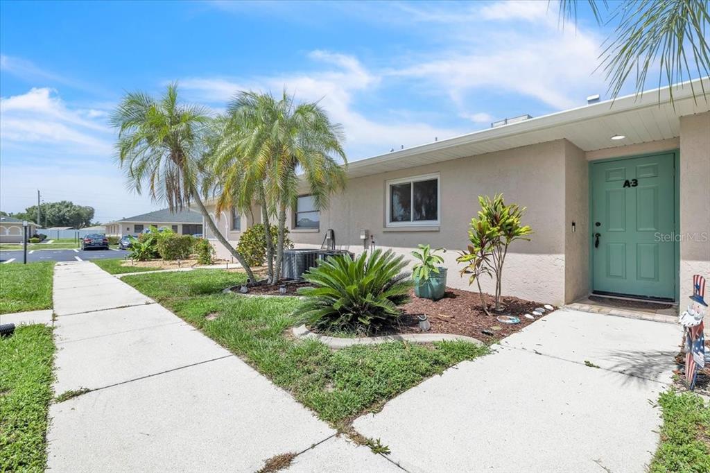 A single-story building exterior features a light-colored facade, a teal front door, and landscaping — 24540 HARBORVIEW ROAD UNIT A3, PUNTA GORDA, FL