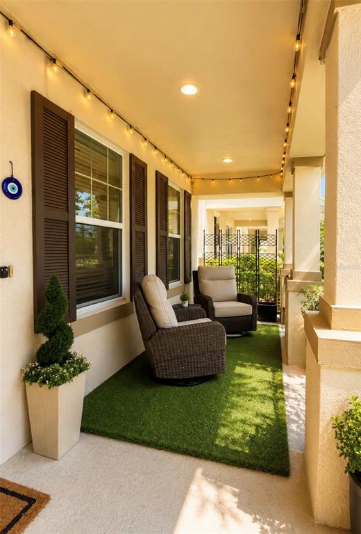 A covered porch features artificial turf, two wicker chairs, and string lights along the ceiling — 8630 POWDER RIDGE TRAIL, WINDERMERE, FL
