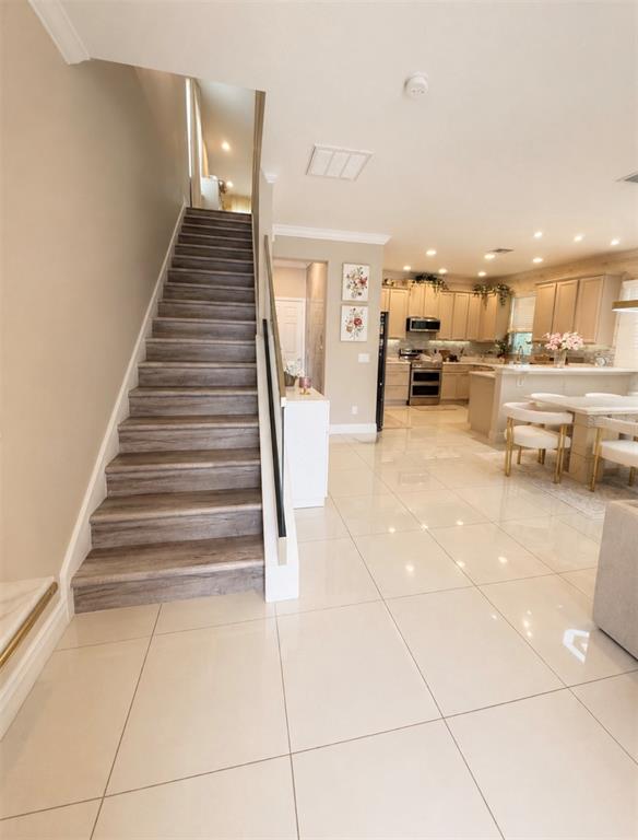 A staircase with wood-look treads leads upward next to a kitchen with light-colored tile flooring — 8630 POWDER RIDGE TRAIL, WINDERMERE, FL
