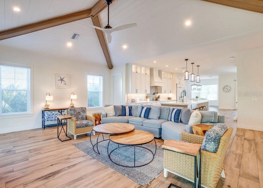 A living room with vaulted ceilings, wood-look flooring, and an open-concept kitchen in the background — 9403 GULF DR, ANNA MARIA, FL