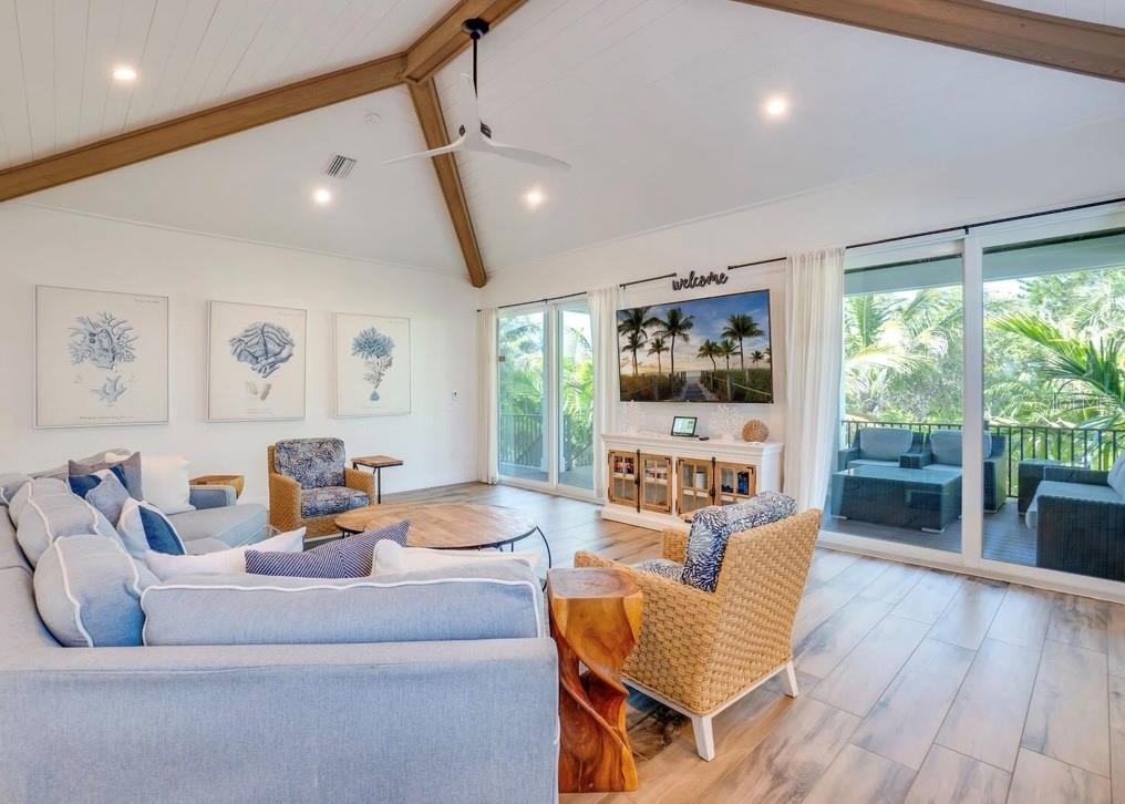 A living room with vaulted ceilings, wood beams, a sectional sofa, and large sliding glass doors — 9403 GULF DR, ANNA MARIA, FL