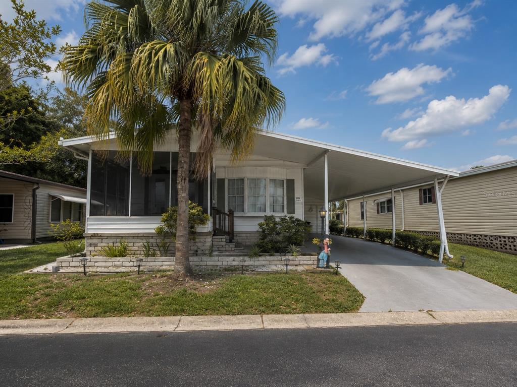 A single-story mobile home with a screened porch, palm tree, and attached carport — 12501 ULMERTON ROAD UNIT 193, LARGO, FL