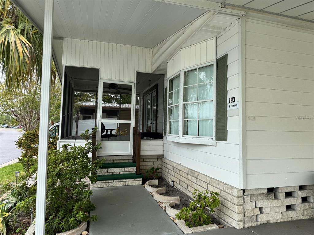 The exterior of a mobile home features a screened-in porch, green steps, and a bay window — 12501 ULMERTON ROAD UNIT 193, LARGO, FL