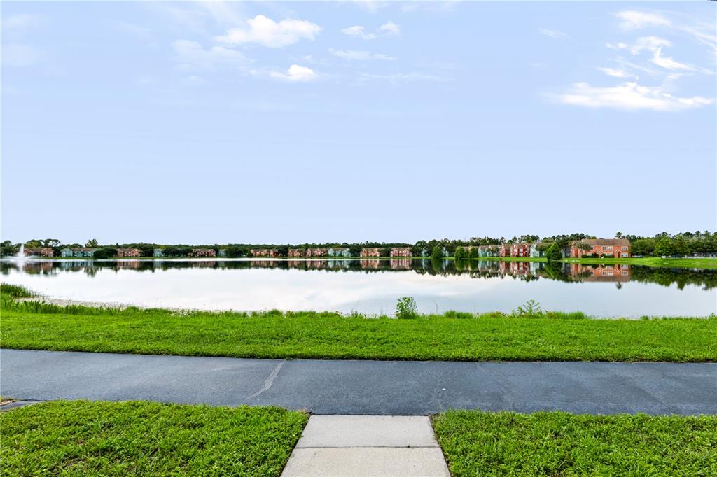 A paved walkway leads to a grassy lawn overlooking a lake with distant apartment buildings — 9818 LAKE CHASE ISLAND WAY UNIT 9818, TAMPA, FL