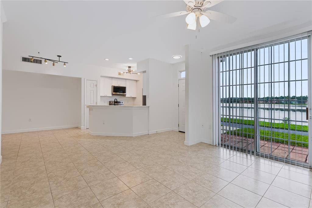 An open-concept living area with tile flooring, a kitchen, and sliding glass doors overlooking water — 9818 LAKE CHASE ISLAND WAY UNIT 9818, TAMPA, FL