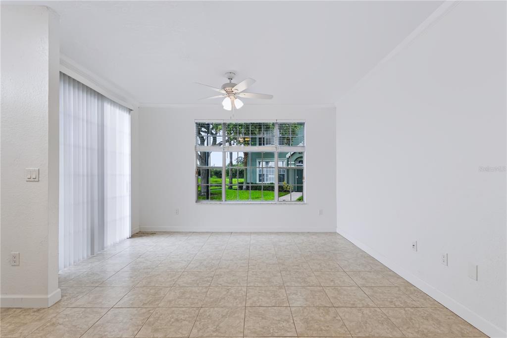 An empty living room features white walls, tile flooring, a ceiling fan, and a large window — 9818 LAKE CHASE ISLAND WAY UNIT 9818, TAMPA, FL