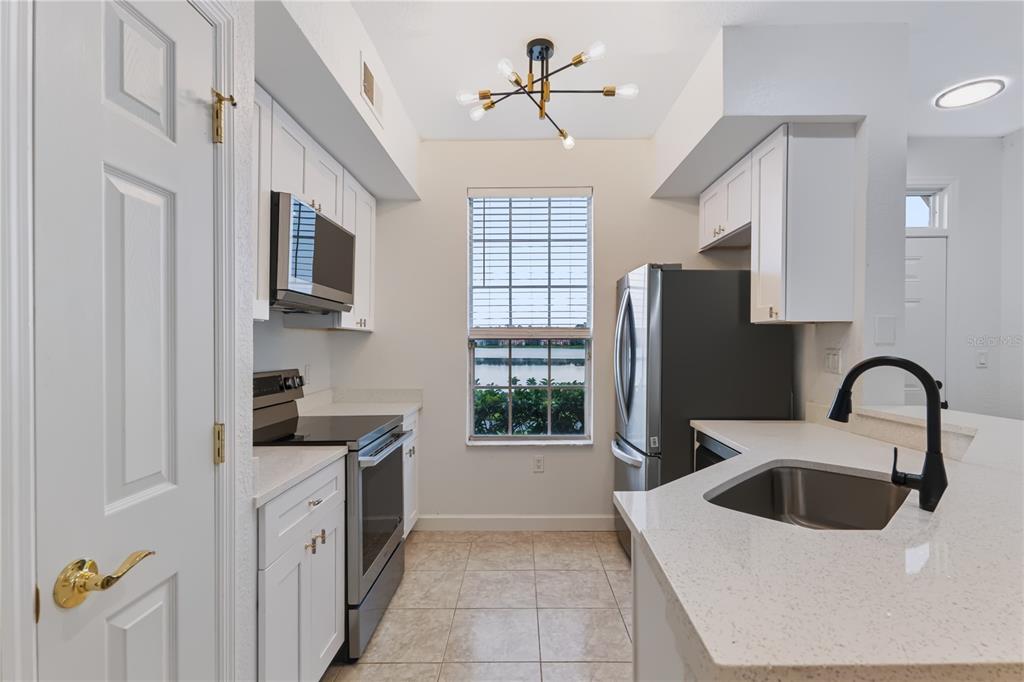 A kitchen features white cabinets, stainless steel appliances, quartz countertops, and a window overlooking water — 9818 LAKE CHASE ISLAND WAY UNIT 9818, TAMPA, FL