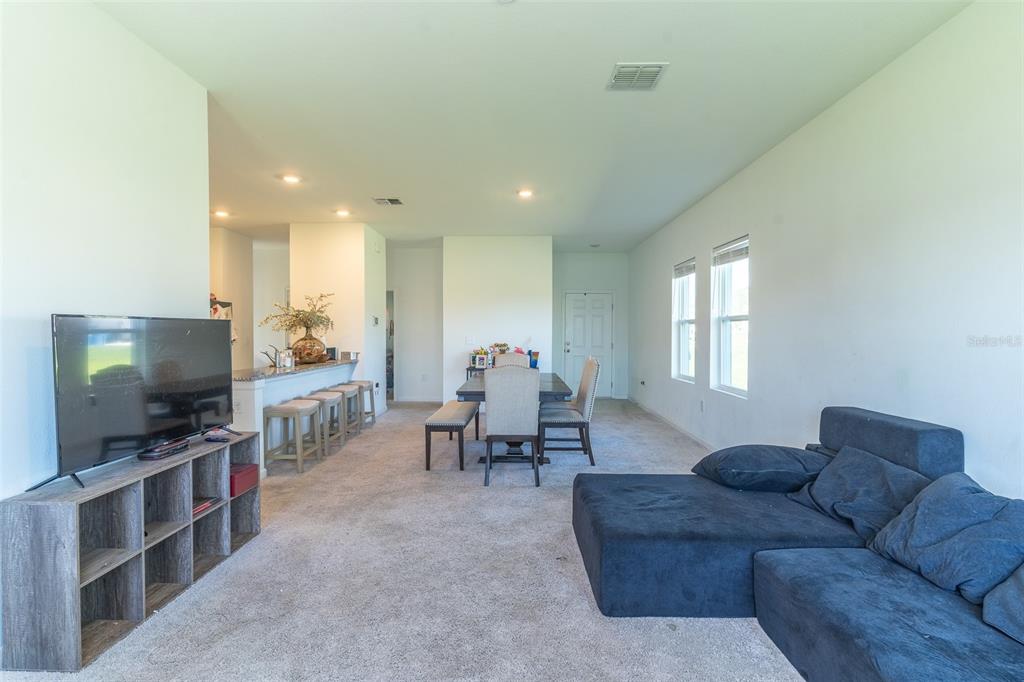 An open-concept living and dining area features carpeted flooring, a dark sectional, and a kitchen island — 436 HENNEPIN LOOP, LAKE WALES, FL