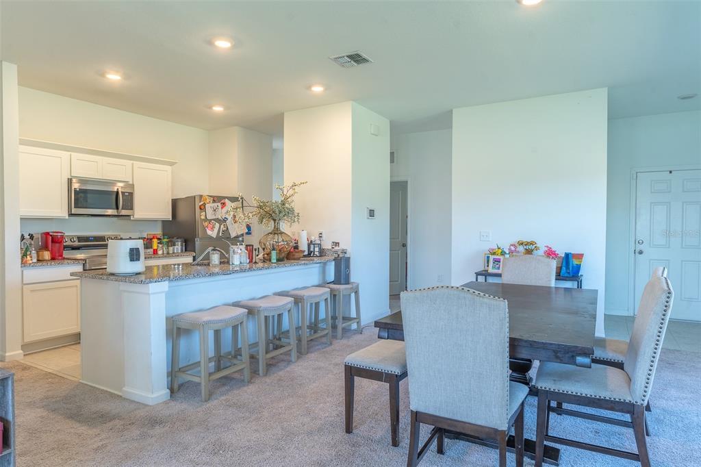 A kitchen with white cabinets and granite countertops opens to a dining area with carpet — 436 HENNEPIN LOOP, LAKE WALES, FL