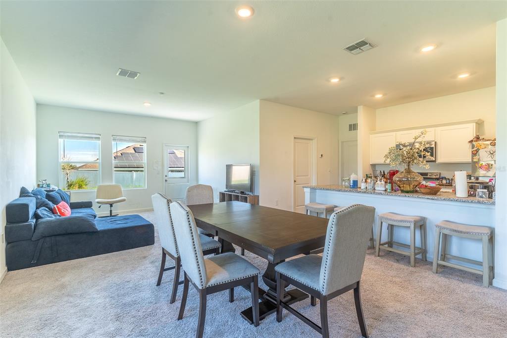 An open-concept living and dining area features a blue sectional, wooden table, and kitchen island — 436 HENNEPIN LOOP, LAKE WALES, FL