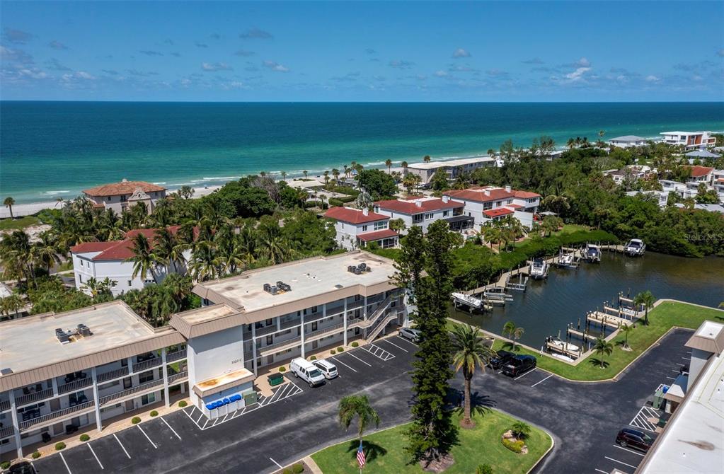 An aerial view shows a multi-story apartment building with a parking lot and boat slips — 3320 GULF OF MEXICO DRIVE UNIT 206C, LONGBOAT KEY, FL