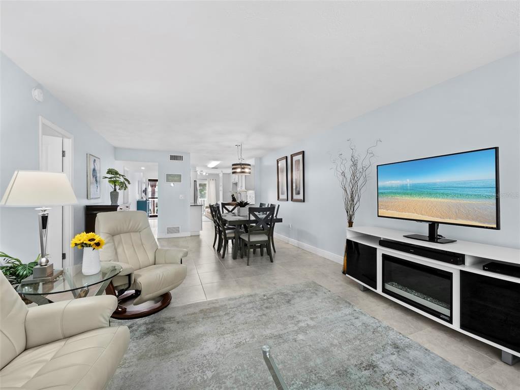 A living room with light blue walls, tile floors, a television, and a dining area beyond — 3320 GULF OF MEXICO DRIVE UNIT 206C, LONGBOAT KEY, FL