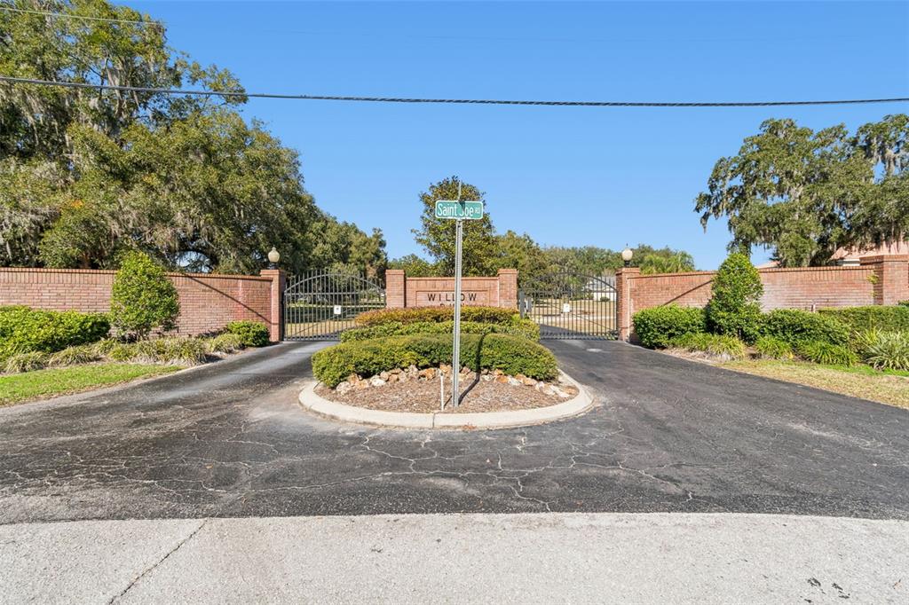 A gated entrance with brick walls and a central landscaped island on a paved road — 14308 WILLOW RUN, DADE CITY, FL