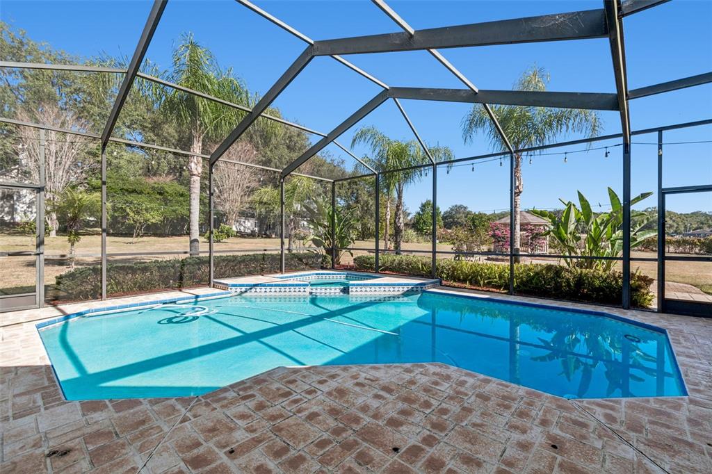A swimming pool and spa are enclosed within a screened lanai with stone paver decking — 14308 WILLOW RUN, DADE CITY, FL