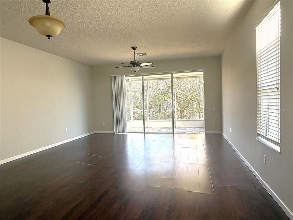 An empty living room features dark wood flooring, a ceiling fan, and sliding glass doors — 26627 CASTLEVIEW WAY, WESLEY CHAPEL, FL