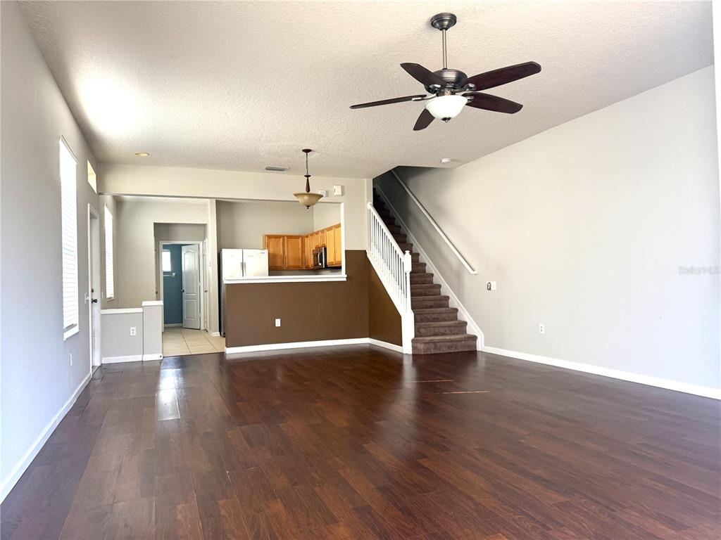 An open living area features dark wood floors, a staircase, and a kitchen with brown walls — 26627 CASTLEVIEW WAY, WESLEY CHAPEL, FL