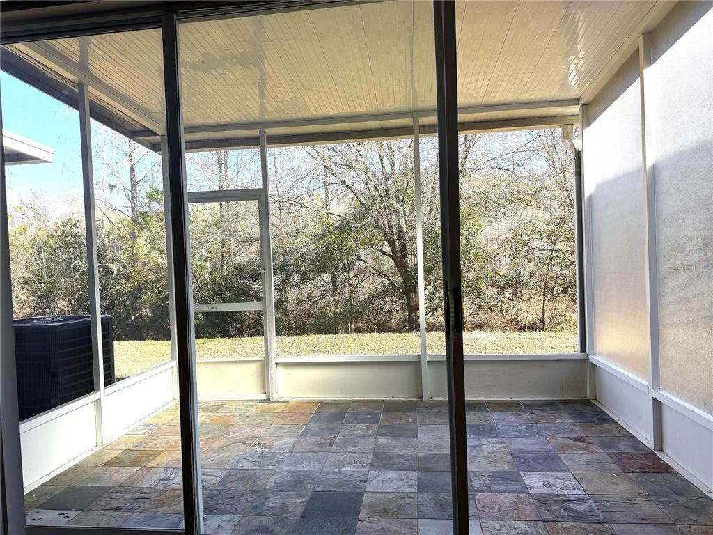 A screened-in porch features multi-colored slate tile flooring and views of a wooded backyard — 26627 CASTLEVIEW WAY, WESLEY CHAPEL, FL