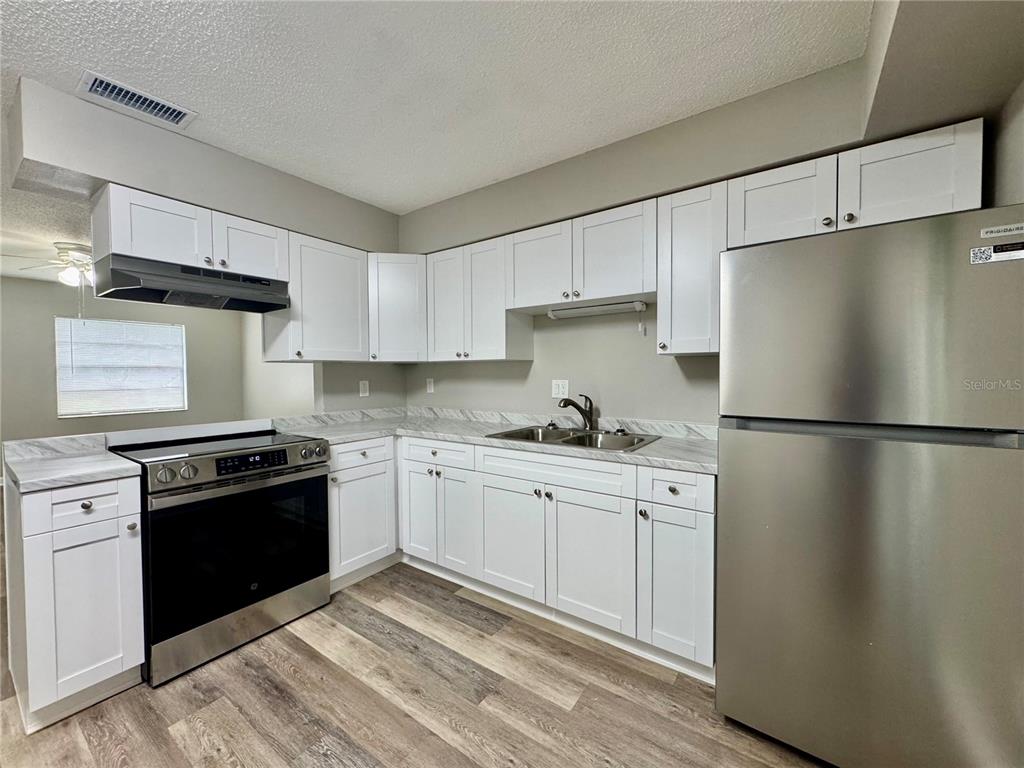 An empty living room features brown walls, wood-look flooring, a ceiling fan, and an open door — 5619 PEACH AVENUE, SEFFNER, FL