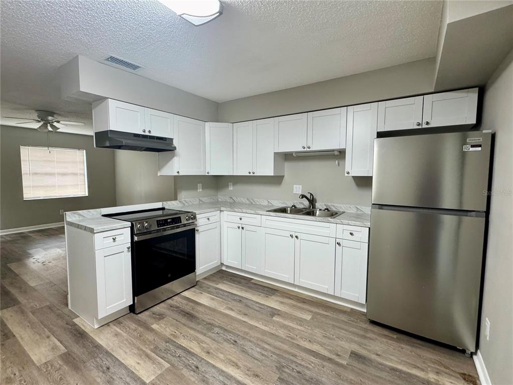 A kitchen features wood-grain cabinets, laminate countertops, black appliances, and wood-look flooring — 5619 PEACH AVENUE, SEFFNER, FL
