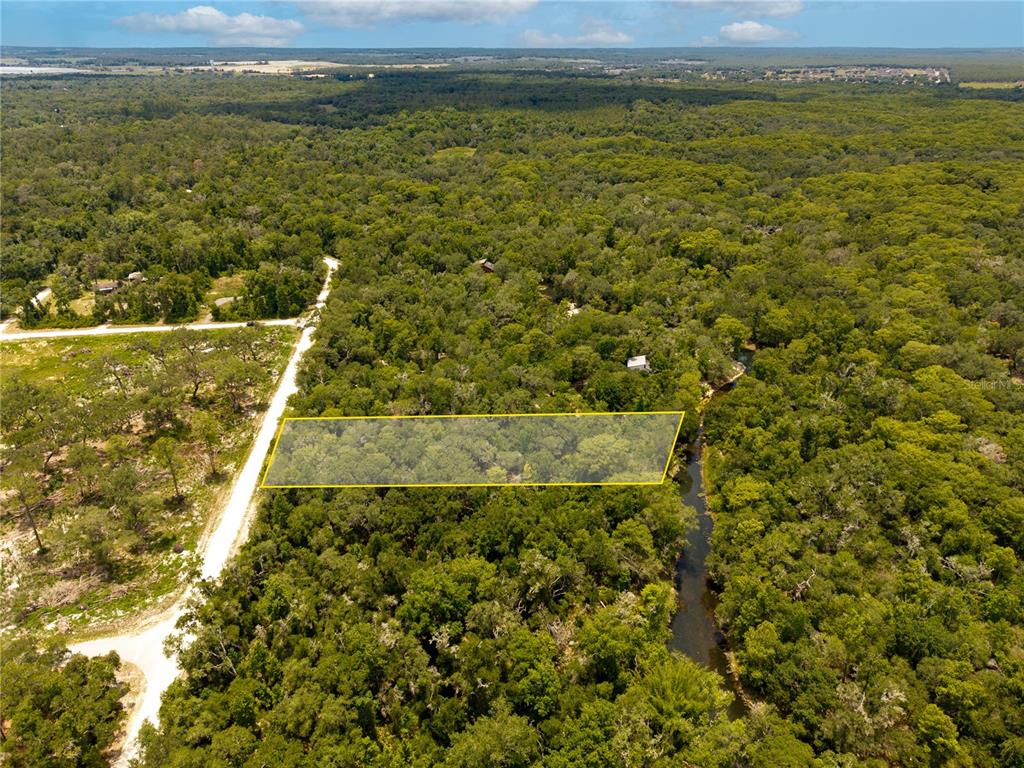 An aerial view shows a rectangular plot of land highlighted in yellow amidst dense forest — 7353 RIVERVIEW DRIVE, WEBSTER, FL